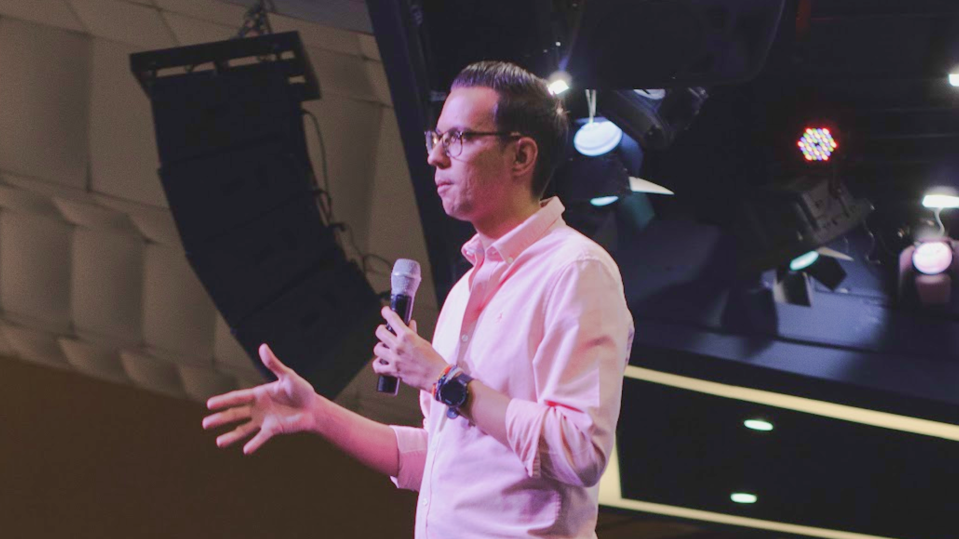 César Rengifo speaking at a public event, holding a microphone and gesturing during a talk.