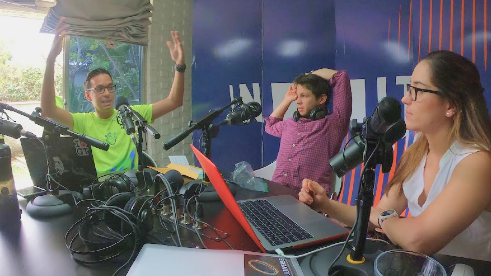 César Rengifo in a podcast studio with two co-hosts, microphones and recording equipment on the table, engaged in discussion at Radio Infinita.