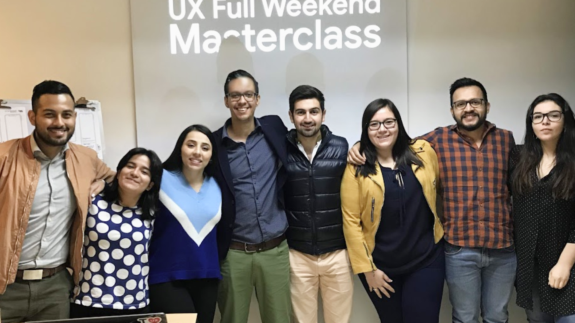 Group photo at UX Full Weekend Masterclass: participants and instructors smiling in front of a screen displaying the event title.